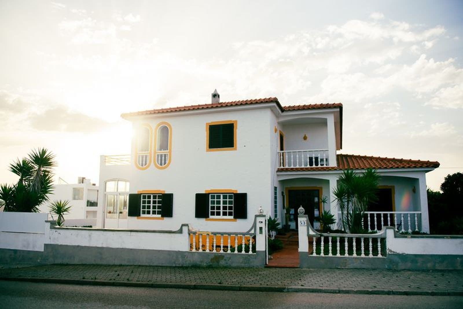 Een huis met een wit hek en witte muren. De zon zit net achter het huis waardoor er een gloed is rond het huis.